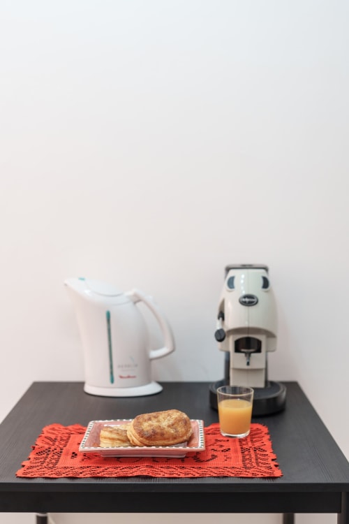 Breakfast setup at Origenes Rooms Procida: pastries, orange juice, electric kettle and coffee machine on black table