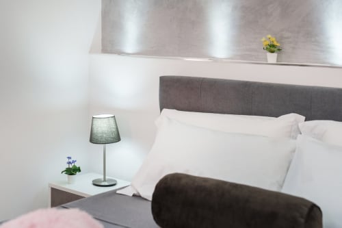 Modern bedroom at Origenes Rooms, Procida with gray upholstered bed, white pillows, bedside lamp, and potted flowers
