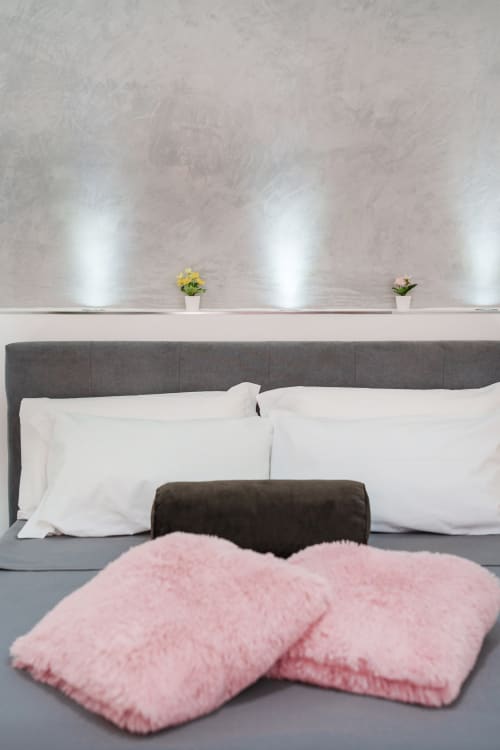 Modern bedroom at Origenes Rooms Procida with gray upholstered bed, white pillows, pink throw pillows, and ambient wall