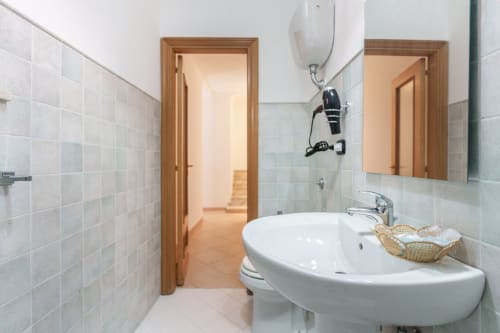 Modern bathroom at Origenes Rooms in Procida with white sink, tiled walls, wooden doors, and shower area