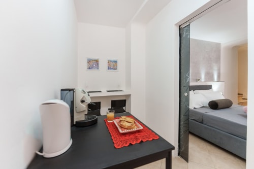 Modern bedroom at Origenes Rooms in Procida with work desk, coffee maker, and en-suite bathroom entrance