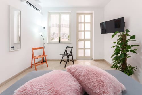 Modern bedroom at Origenes Rooms, Procida with pink poufs, orange and black chairs, flat-screen TV, and green plant decor
