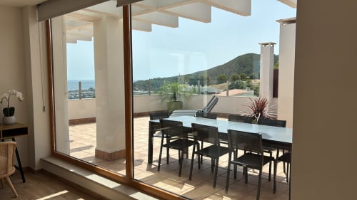 Panoramic penthouse terrace in Sesimbra with sea views, dining table, and coastal mountains visible from covered balcony.