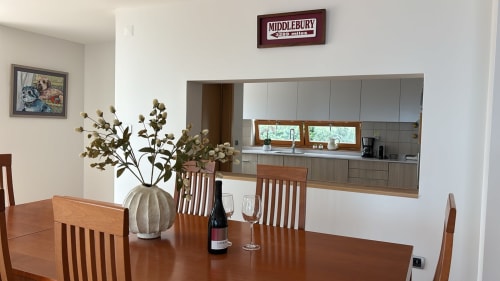Dining area in Sesimbra penthouse with wooden table, chairs, wine bottle, and view into modern kitchen