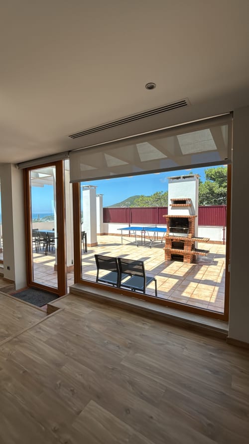 Panoramic penthouse interior with large glass doors opening to sea view terrace, pool, and brick fireplace in Sesimbra,