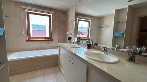 Luxurious bathroom in Sesimbra penthouse with dual sinks, bathtub, windows overlooking sea and town