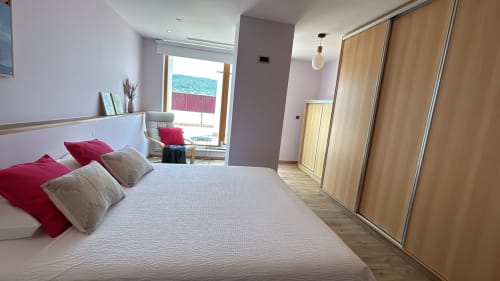 Modern bedroom in Sesimbra penthouse with sea view, white bed with red pillows, wood furnishings, balcony access