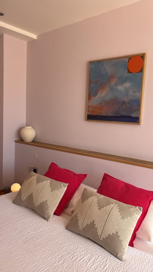 Modern bedroom at Sesimbra Sun Sea penthouse with pink walls, red pillows, framed seascape artwork with orange sun, and white