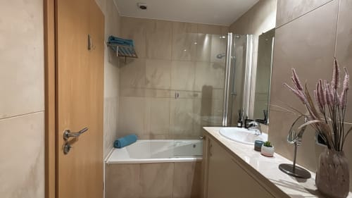 Modern bathroom in Sesimbra penthouse with white sink, glass shower enclosure, and decorative purple flowers on vanity