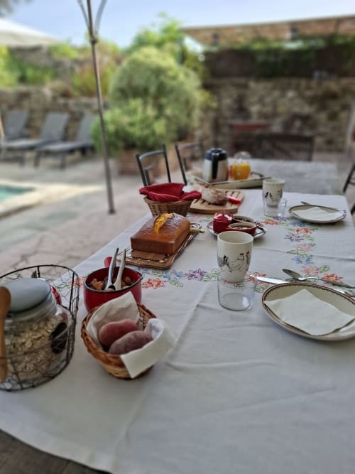 Outdoor breakfast table at Les Gravets B&B in Sigalens with cake, pastries, and coffee service in a rustic courtyard setting.