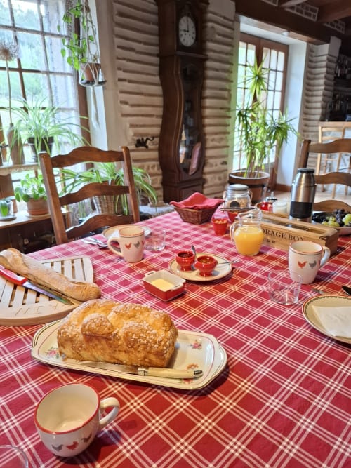 Mesa rústica de desayuno en Les Gravets B&B en Sigalens con pasteles frescos, zumo y mantel a cuadros rojos