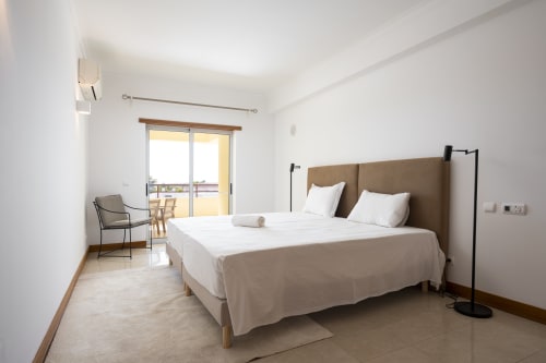 Quarto espaçoso no RB Algarve Vilamoura com cama de casal, cabeceira em bege, varanda com vista para a piscina e comodidades modernas
