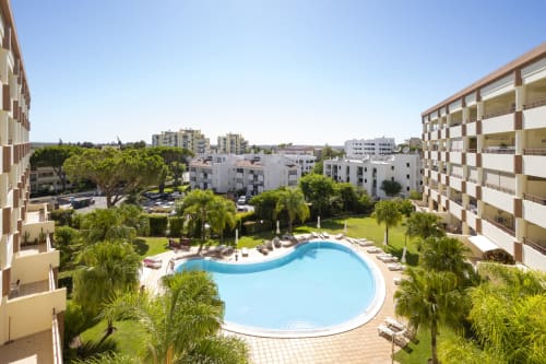 Área de piscina do hotel RB Algarve em Vilamoura com apartamentos, palmeiras e espreguiçadeiras