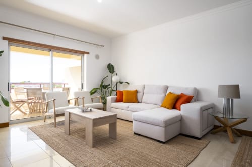 Sala de estar moderna e luminosa no RB Algarve Vilamoura com sofá branco, móveis em madeira, acesso ao terraço e vista para a piscina