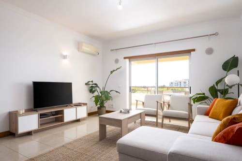 Sala de estar moderna no RB Algarve Vilamoura com TV inteligente, assentos confortáveis, plantas e vista para piscina de varanda