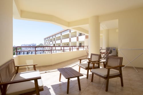 Terraço ensolarado do apartamento RB Algarve Vilamoura com móveis em madeira e vista para edifícios residenciais