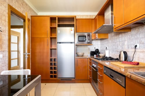 Cozinha moderna no apartamento DANI do RB Algarve Vilamoura com armários laranja, eletrodomésticos em aço inoxidável e acabamentos em madeira