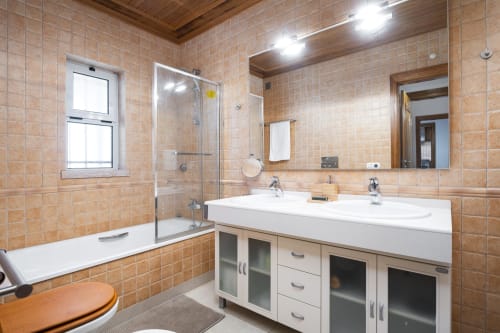 Banheiro moderno no RB Algarve Vilamoura com azulejos pêssego, lavabo de dupla pia, box de vidro e teto de madeira