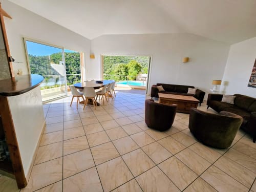 Villa Eva's spacious open-plan living area with sea views, dining table, lounge seating, and access to pool terrace in Favone