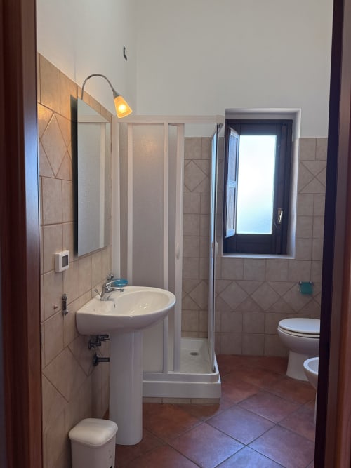 Ampio bagno a Borgo Luce con lavabo a colonna, box doccia, finestra e pareti piastrellate a Francavilla Marittima