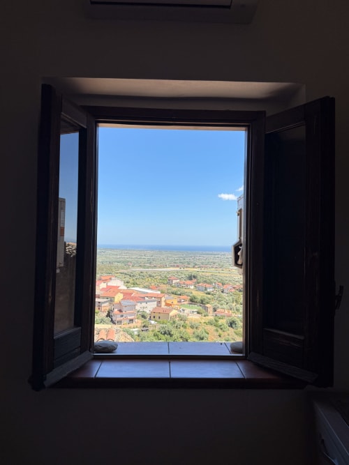 Finestra nera aperta sulla vista del villaggio costiero italiano di Borgo Luce a Francavilla Marittima con edifici dai tetti rossi