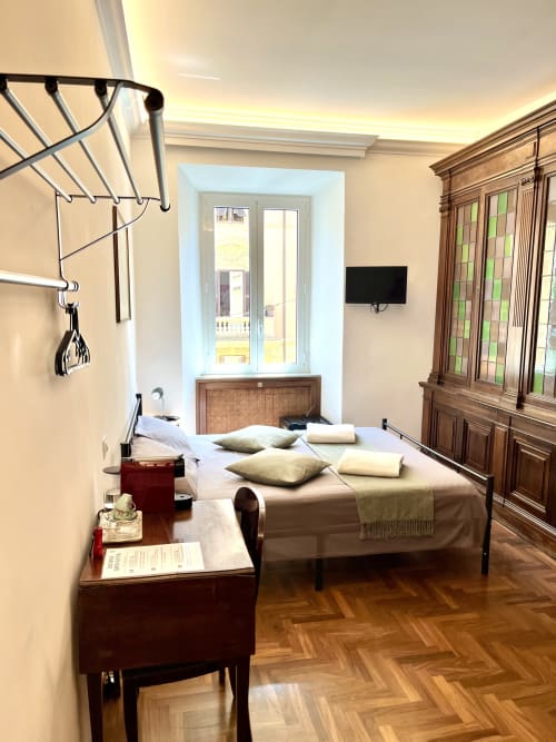 Camera da letto Domus Giovanna Roma con letto matrimoniale, guardaroba in legno, scrivania, TV e finestra con vista su monumenti