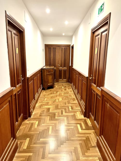 Elegante corridoio di Domus Giovanna a Roma con porte in legno, pavimento in parquet a spina di pesce e pareti bianche