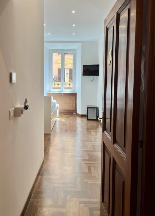 Elegante corridoio della Domus Giovanna Roma B&B con parquet a spina di pesce, porte in legno scuro e finestre con vista sulla città