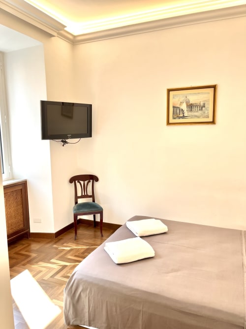 Luminosa camera familiare presso Domus Giovanna B&B a Roma con letto, TV, sedia in legno e pavimento in parquet