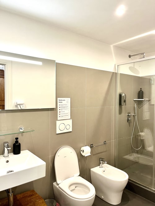 Bagno moderno a Domus Giovanna Roma con sanitari bianchi, doccia in vetro, bidet e piastrelle beige