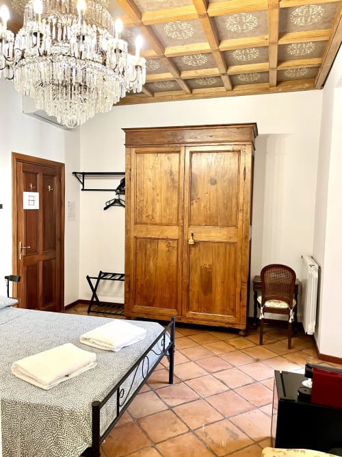 Camera da letto rustica a Domus Giovanna Rome B&B con letto in ferro battuto, guardaroba in legno, lampadario in cristallo e pavimento in cotto