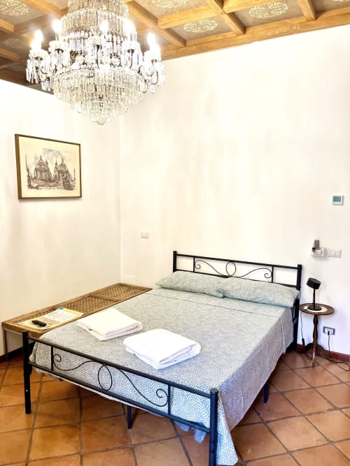 Camera da letto rustica elegante presso Domus Giovanna B&B a Roma con lampadario in cristallo, letto in ferro battuto e arte murale classica