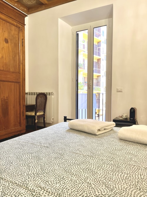 Camera da letto rustica alla Domus Giovanna Roma con copriletto decorato, porta in legno e balcone vista cortile interno