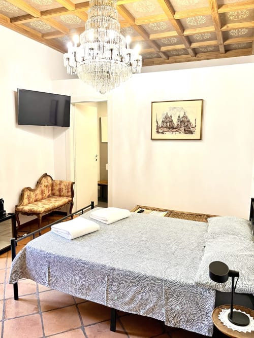 Camera da letto rustica di Domus Giovanna Roma B&B con letto, lampadario ornato, divano vintage, TV e arredi classici