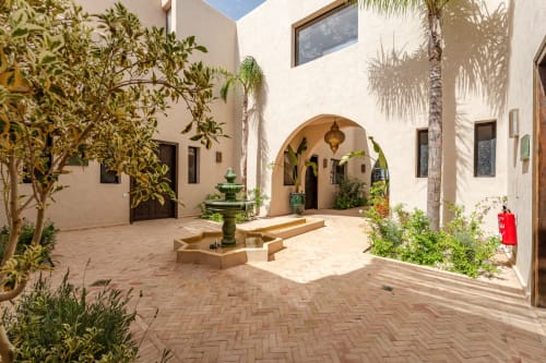 Cour du Riad Arkaya à Essaouira avec carrelage en terre cuite, porte cintrée, palmiers et fontaine ornementale