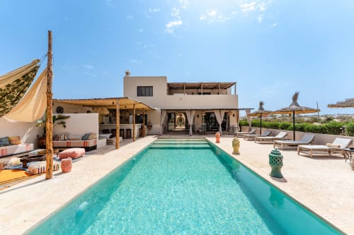 La piscine turquoise et la terrasse de la Riad Arkaya avec villa blanche, transats et vue sur le paysage d'Essaouira