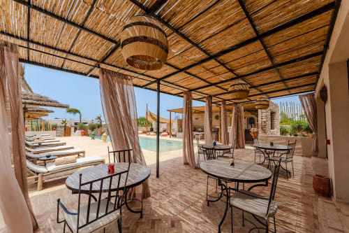 Terrasse ombragée du Riad Arkaya à Essaouira avec pergola en bois, rideaux flottants, tables à manger et bassin