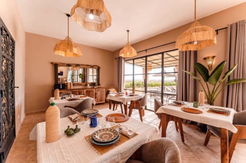 Élégante salle à manger du Riad Arkaya à Essaouira avec luminaires suspendus en bois, murs en terre cuite et vue sur l'océan