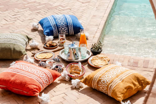 Petit-déjeuner au bord de la piscine du Riad Arkaya Essaouira avec coussins colorés, pâtisseries traditionnelles et piscine turquoise