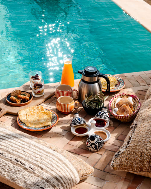 Petit-déjeuner en bord de piscine au Riad Arkaya d'Essaouira avec pâtisseries marocaines, jus d'orange et eau turquoise