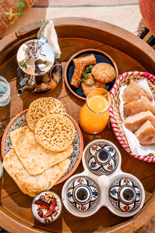 Petit-déjeuner marocain traditionnel au Riad Arkaya à Essaouira avec crêpes, pâtisseries, jus d'orange et condiments épicés