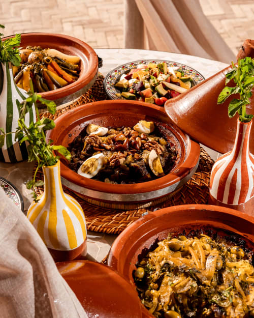 Plats de tajine marocain traditionnels au Riad Arkaya à Essaouira avec herbes fraîches et poterie décorative