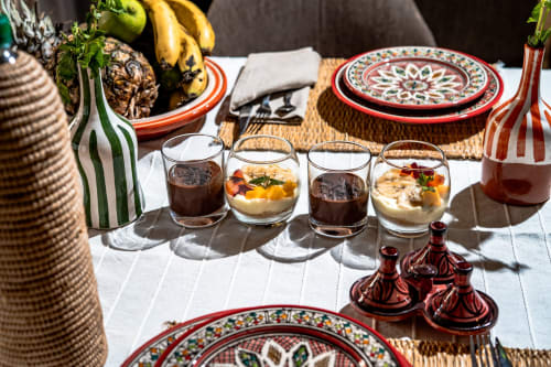 Mise de table marocaine au Riad Arkaya à Essaouira avec assiettes traditionnelles rouges et blanches, fruits frais et desserts