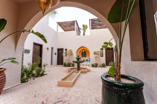 La cour tranquille du Riad Arkaya à Essaouira accueille une fontaine centrale, une porte voûtée et des plantes en pots luxuriantes