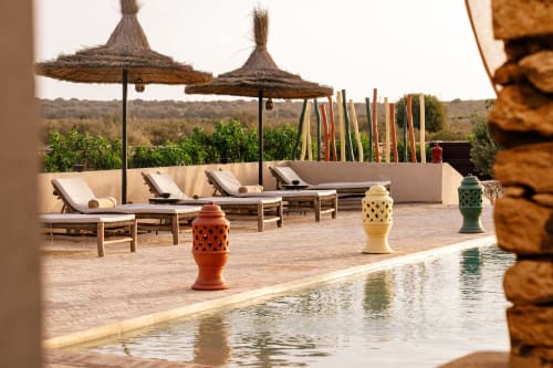Espace piscine sur le toit du Riad Arkaya à Essaouira avec chaises longues, parasols en chaume et fontaines en céramique marocaine