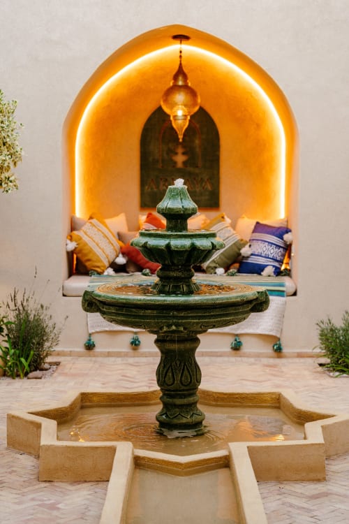 Fontaine ornementale verte dans la cour du Riad Arkaya à Essaouira, avec alcôve voûtée illuminée et coussins colorés