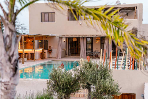 L'hôtel Riad Arkaya à Essaouira offre une cour avec piscine moderne, eau turquoise, architecture beige et palmiers