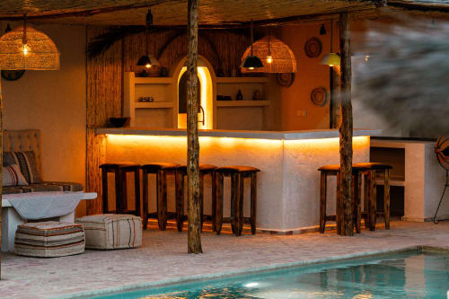 Bar piscine du Riad Arkaya à Essaouira avec éclairage chaleureux, accents en bois, sièges de bar et décor marocain au crépuscule