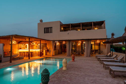 Vue crépusculaire du Riad Arkaya avec piscine illuminée, transats et terrasse à Essaouira