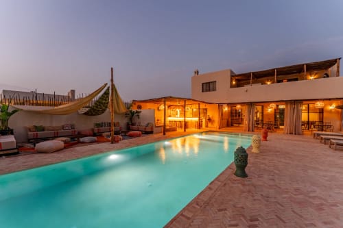 Hôtel Riad Arkaya à Essaouira avec sa piscine turquoise, patio en terre cuite et architecture marocaine illuminée au crépuscule